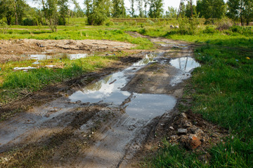 The harsh landscape nature and road through the fields for the off-road SUV with puddles and mud. Autumn or spring background. Forest in the background. Rain-washed road, is impassable, slush, mud