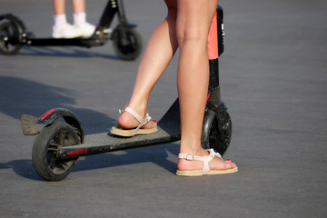 Girl rides an electric scooter on a city street, slim female legs on asphalt. Riding e-scooter in...