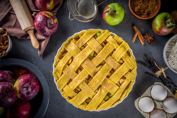 Autumn apple pAutumn apple pie cooking background. Baking background with raw traditional classic apple pie, baking ingredients and utensils, black concrete background copy spaceie cooking background