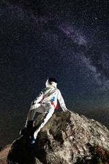 Astronaut resting on top of rocky mountain under beautiful night sky with stars. Astronaut wearing white space suit with helmet. Concept of space exploration, cosmonautics and milky way. © anatoliy_gleb