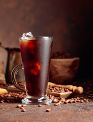 Ice coffee in dammed glass and coffee beans on an old brown table with kitchen utensils.