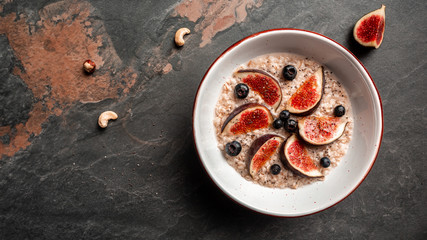 Delicious and healthy oatmeal with figs, blueberries and chia seeds on a dark background. Gluten free, lactose free, top view