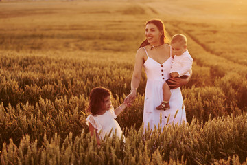 Cheerful family of mother, little son and daughter spending free time on the field at sunny day time of summer