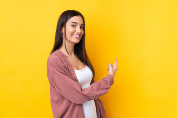 Young brunette woman over isolated yellow background pointing back