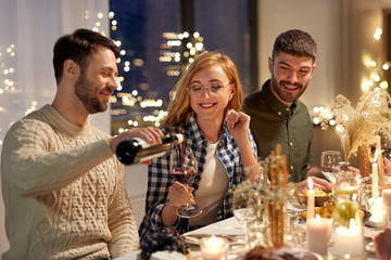 holidays and celebration concept - happy friends having christmas dinner at home pouring red wine