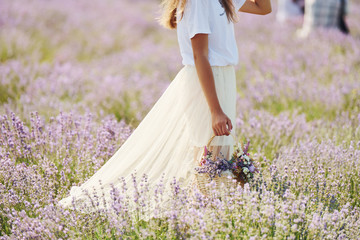 Close up view of woman in beautiful white dress that using basket to collect lavender in the field
