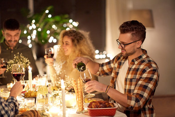 holidays and celebration concept - happy young man pouring non-alcoholic red wine to glass at christmas dinner party at home