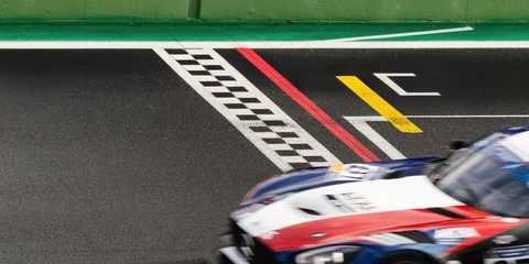 The finish line of a racing track with a fast sport car crossing it alone at high speed with a blurred motion