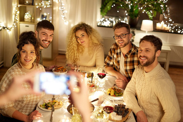 holidays, celebration and people concept - happy friends being photographed with smartphone at home christmas dinner party