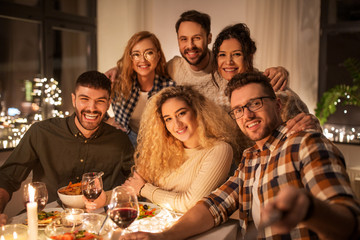 holidays, celebration and people concept - happy friends taking selfie at home christmas dinner party