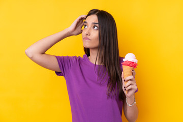 Young brunette woman with a cornet ice cream over isolated yellow background having doubts and with confuse face expression