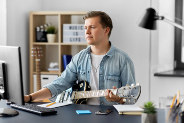 leisure, music and people concept - young man or musician with computer playing guitar sitting at table at home