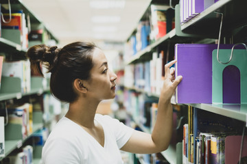 Young Asian women are searching for books and reading from the bookshelves in the college library to research and develop themselves in education