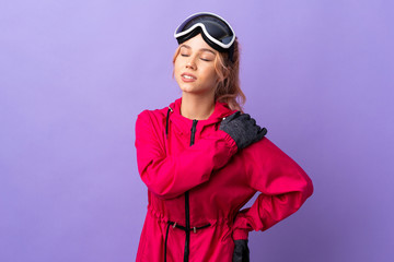 Skier teenager girl with snowboarding glasses over isolated purple background suffering from pain in shoulder for having made an effort