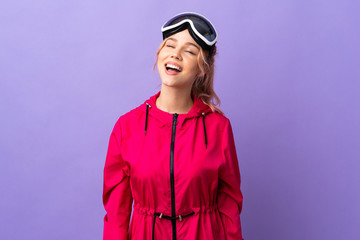Skier teenager girl with snowboarding glasses over isolated purple background laughing