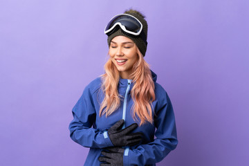 Skier teenager girl with snowboarding glasses over isolated purple background smiling a lot