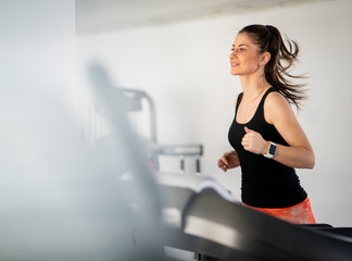 Naklejka na ściany i meble Athletic pretty woman using treadmill in gym