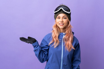 Skier teenager girl with snowboarding glasses over isolated purple background holding copyspace imaginary on the palm to insert an ad