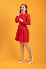 Full length portrait of a happy asian woman using mobile phone isolated over orange background.