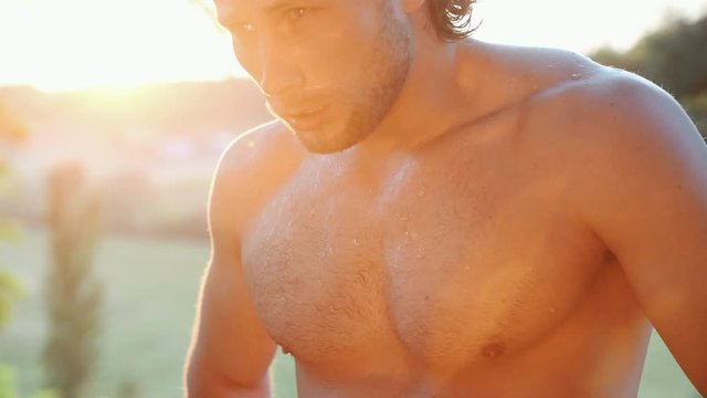 Close up view of tired and sweating handsome shirtless man illuminated by bright sunlight.