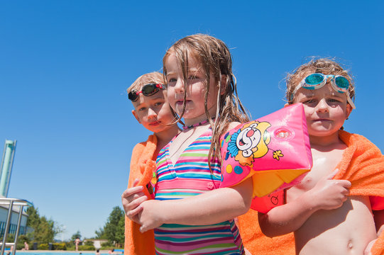 drei Kinder in Badesachen mit orangem Badetuch