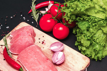 Raw juicy meat steaks ready for roasting on a black chalk board background. fillet with cherry tomatoes, hot pepper and herbs.