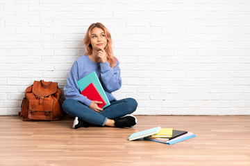 Teenager student woman with pink hair sitting on the floor at indoors thinking an idea while looking up