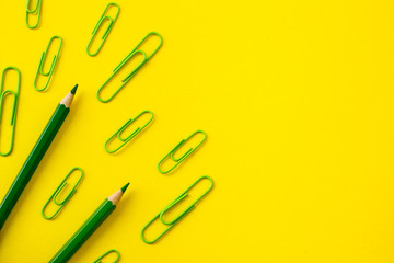 green paper clips and pencils lying on yellow background