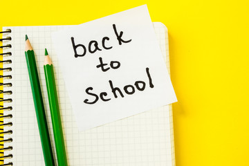 note sheet with paper clip and pencils on yellow background back to school