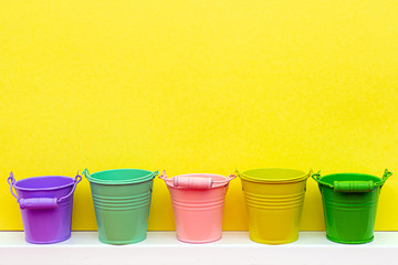 Five multi-colored buckets on a yellow background with place for text, yellow, pink, red, green, turquoise buckets, gardening concept, colored on yellow background
