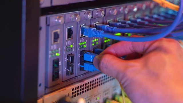 man working in network server room with fiber optic hub for digital communications and internet.