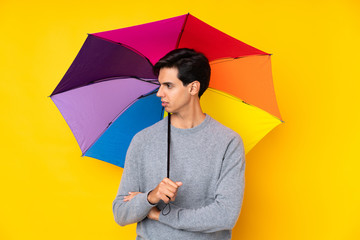 Man holding an umbrella over isolated yellow background looking side