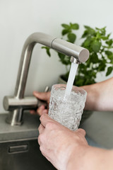 Person, die sich am Wasserhahn ein Glas mit Leitungswasser befüllt
