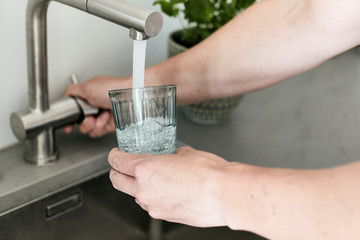 Person, die sich am Wasserhahn ein Glas mit Leitungswasser befüllt