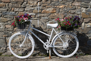 Fototapeta na wymiar White painted decorative bicycle with flowers against stone wall