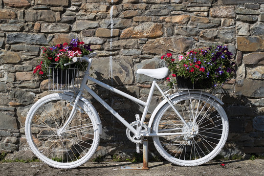 White painted decorative bicycle with flowers against stone wall