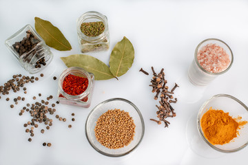 various spices in glass bowls and jars on a white background