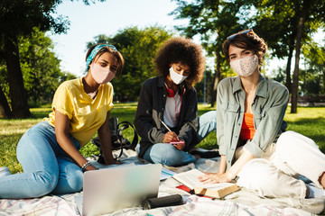Image of multinational women doing homework with laptop in summer park