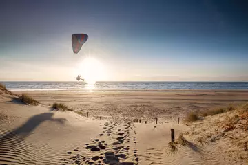 Poster de jardin Mer du Nord, Pays-Bas man paragliding on beach at sunset