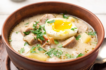 Traditional Polish sour soup Zurek in ceramic bowl on rustic wooden background