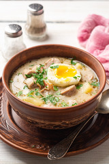 Traditional Polish sour soup Zurek in ceramic bowl on rustic wooden background