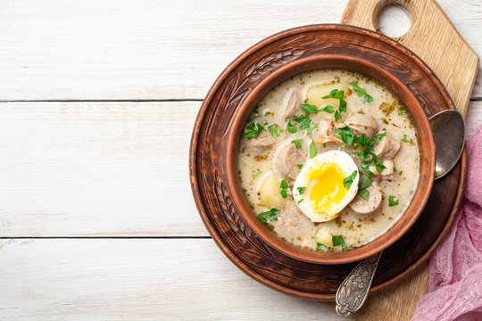 Traditional Polish sour soup Zurek in ceramic bowl on rustic wooden background