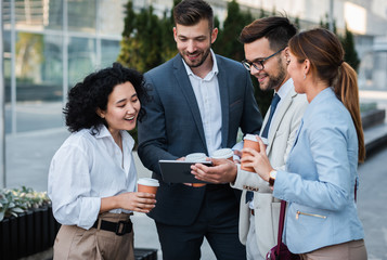 Team of  business people standing outside in front of office buildings talking and having coffee brake.
