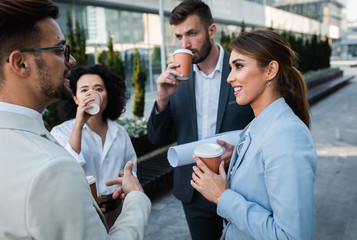Team of  business people standing outside in front of office buildings talking and having coffee brake.