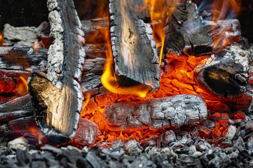 Burning oak wood in Russian stove. Stove in country house. Bright flame over hot coals. Close-up. Embers glow against blurred orange flame background. Selective focus.