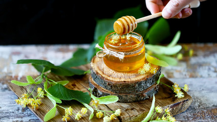 Selective focus. Honey stick, jar of linden honey, linden flowers. Linden honey.
