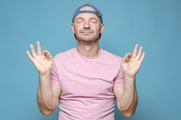 Cute man shows ok gesture with two hands and stands calmly with closed eyes. Everything is fine. 