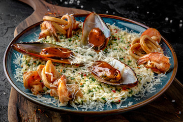 Delicious risotto with seafood mussels, tiger prawns. Beautiful serving in a blue plate on a wooden board.
