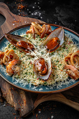 Delicious risotto with seafood mussels, tiger prawns. Beautiful serving in a blue plate on a wooden board.