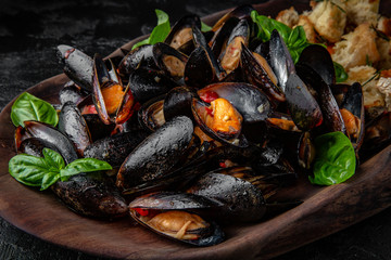 Delicious cooked mussels in sauce with dried baguette. Sea food serving in a wooden plateau